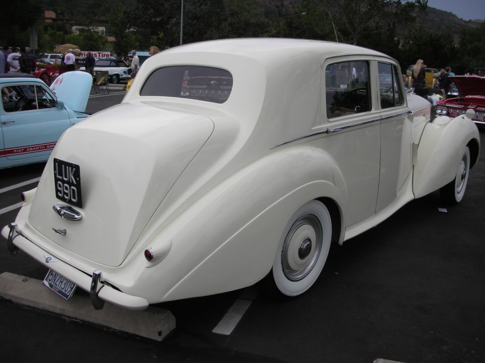 White sedan with a rounded rear, chrome bumper, and whitewall tires. License plate reads LUK 990