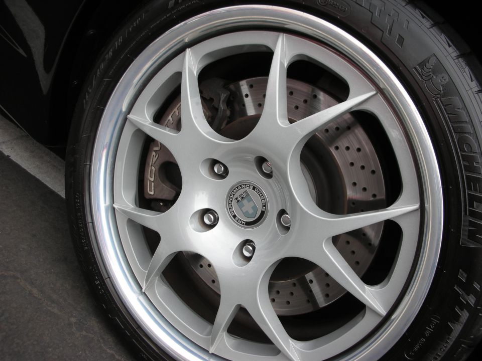 Close-up of a silver multi-spoke alloy wheel with drilled brake rotors and 'CORV' caliper text. Tire has Michelin branding
