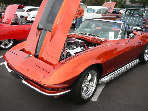 1992 Ford Crown Victoria - This orange convertible, likely a 1967 Chevrolet Corvette, displays its chrome engine and side pipes with the hood open at a car show.