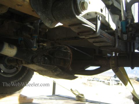 1990 Ford Bronco - Underbody view of a vehicle's solid rear axle, differential and leaf springs with blue shocks, photographed from below on a trailer.