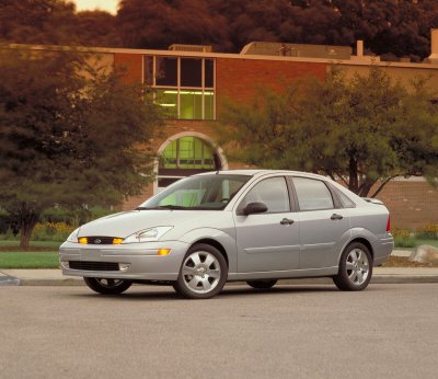 2002 Ford Focus - This silver 2002 Ford Focus sedan is seen from a three-quarter front view, parked on pavement with a brick building in the background.