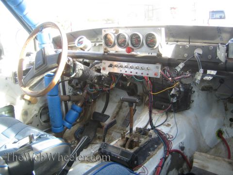 1990 Ford Bronco - Stripped interior of a race car showing a roll cage, wood-rim steering wheel, a panel of aftermarket gauges and exposed wiring.