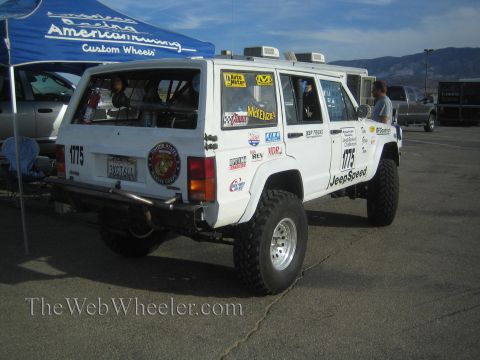 1990 Ford Bronco - Rear view of a white Jeep Cherokee race SUV numbered 1775 parked under an American Racing canopy with people and mountains behind.