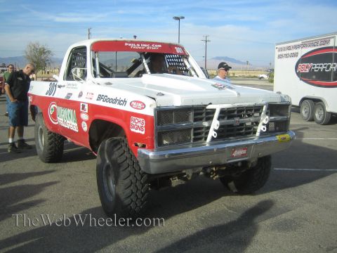 1990 Ford Bronco - white and red square-body Chevrolet race pickup numbered 301 with a chrome tube bumper sits in a paved lot near a Poly Performance trailer.