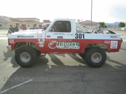 1990 Ford Bronco - red-and-white off-road race truck numbered 301, lettered California Tomatoes and BFGoodrich, parked on pavement at a desert event.