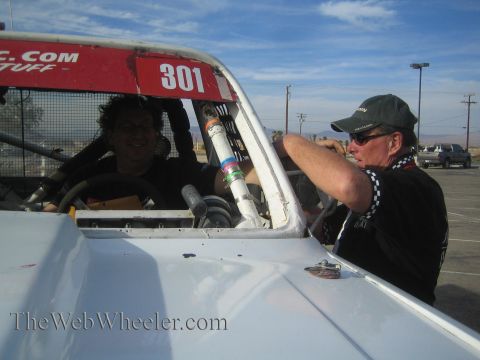 1990 Ford Bronco - Two men converse at the open cockpit of a white race truck numbered 301, one seated inside, the other leaning on the hood in a ball cap.