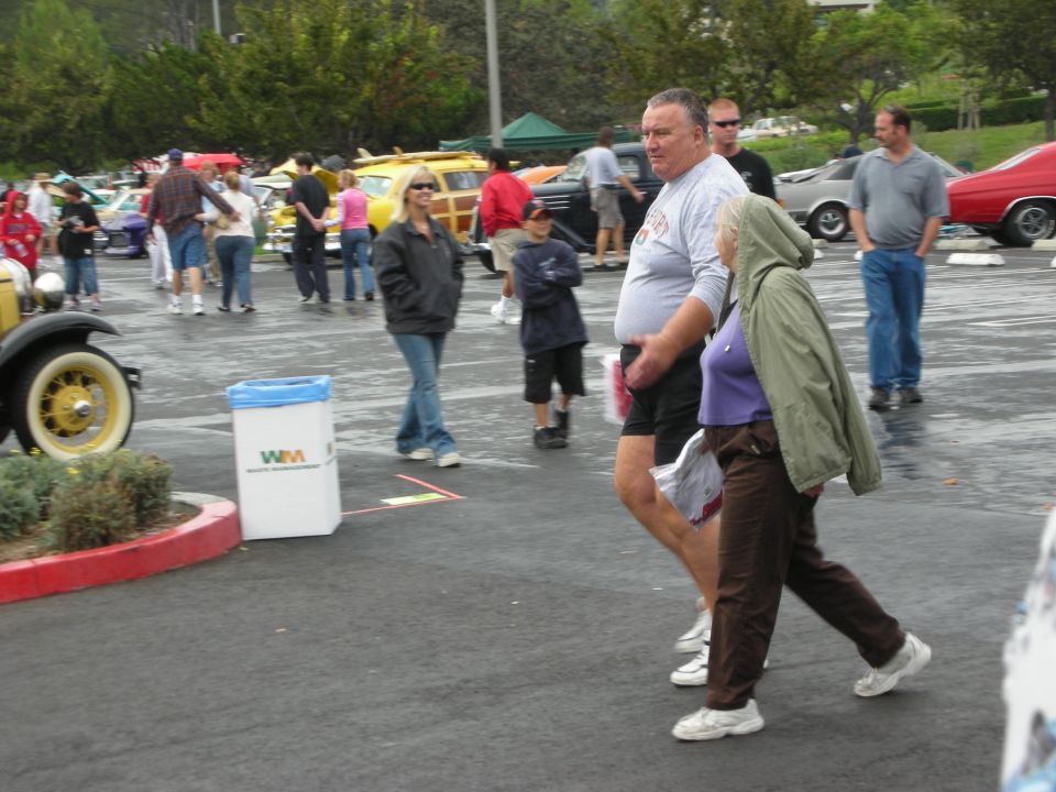 People walking at an outdoor car show with various vehicles in the background