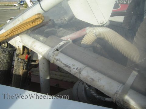 1990 Ford Bronco - Detail of a race vehicle's roll-cage tubing, reservoir shocks and flexible hoses behind a dusty white body panel.