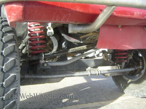 1990 Ford Bronco - Underbody shot of a lifted red vehicle showing red coil springs, a solid axle, sway bar and steering linkage between the tires.