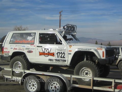 1990 Ford Bronco - white Jeep Cherokee JeepSpeed racer numbered 1722 with Morphic and Full Traction livery and a roof light bar, loaded on a trailer.