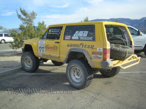 1990 Ford Bronco - yellow Jeep Cherokee JeepSpeed racer numbered 1717 with Goodyear and Rubicon Express decals and a rear spare tire, parked outdoors.