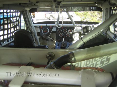 1990 Ford Bronco - View into a caged race vehicle's stripped interior with a dash of gauges, shifter and roll bars, looking forward through the cabin.