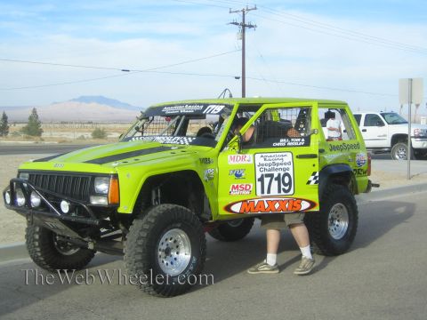 1990 Ford Bronco - bright green Jeep Cherokee JeepSpeed racer numbered 1719 with Maxxis and MSD livery, tube bumper and lift, with a person beside it.