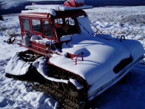 2000 Ford E350 - A red snowcat vehicle sits partially covered in snow on a cold, overcast day.
