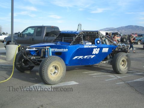 1990 Ford Bronco - Side view of a blue tube-frame off-road race buggy numbered 168 with BFGoodrich decals, parked beside a pickup at a desert event.
