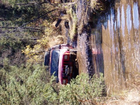 2000 Ford E350 - A red Jeep Cherokee is stuck in a muddy, watery ditch surrounded by trees and brush.