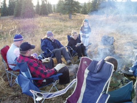 2000 Ford E350 - A group of people enjoy a campfire in a natural setting, with trees and dry grass surrounding them.