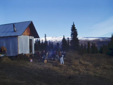 2000 Ford E350 - People enjoy a campfire outside a rustic cabin with a scenic mountain backdrop.