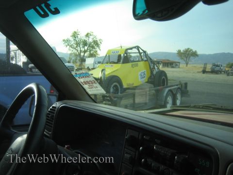 1990 Ford Bronco - yellow off-road race car numbered 1635 loaded on a trailer, viewed through the windshield and dashboard of a parked vehicle.