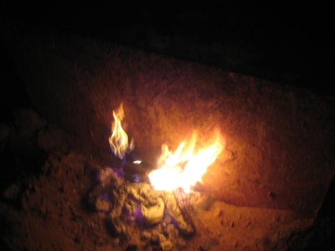 1990 Ford Bronco - small white-orange flame burning at the base of a dark earthen fire pit at night.