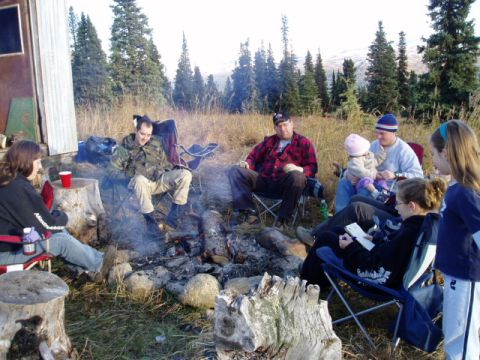 2000 Ford E350 - People enjoy a campfire gathering in a natural outdoor setting with trees and dry grass.