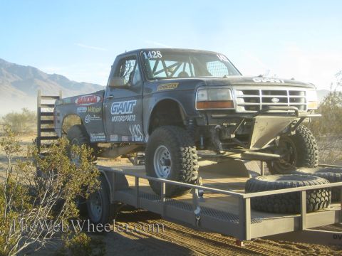 1990 Ford Bronco - dark Ford off-road race truck marked Giant Motorsports and number 1428 sitting on a flatbed trailer in the desert.