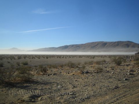 1990 Ford Bronco - wide desert valley with low dust hanging over the basin and a mountain ridge under a clear blue sky.