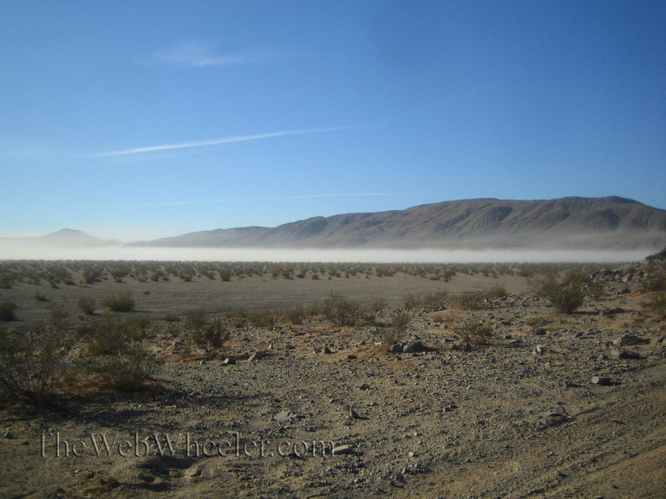 Desert landscape with low dust haze across a valley and mountains under blue sky