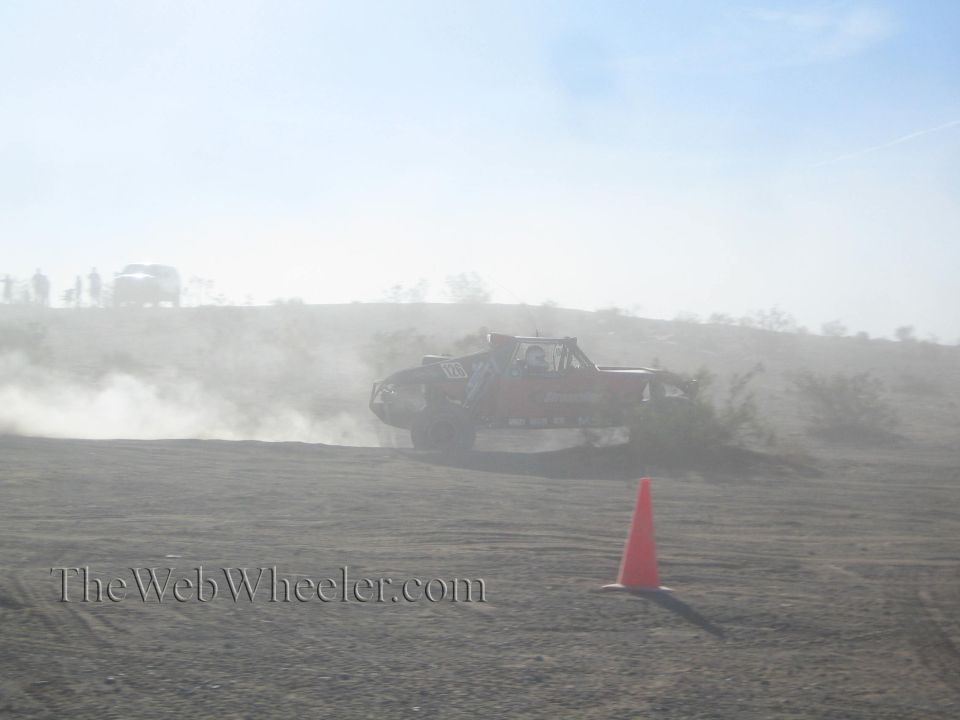 Off-road race truck kicking up dust on a desert course near an orange cone