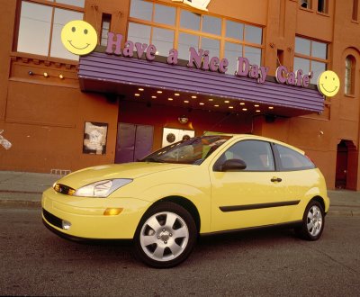 2002 Ford Focus - A yellow 2002 Ford Focus is parked in front of a building with a sign that says "Have a Nice Day Cafe".