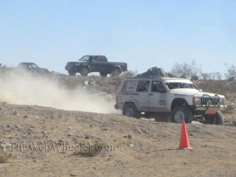 White Jeep Cherokee race vehicle speeding across a rocky desert course