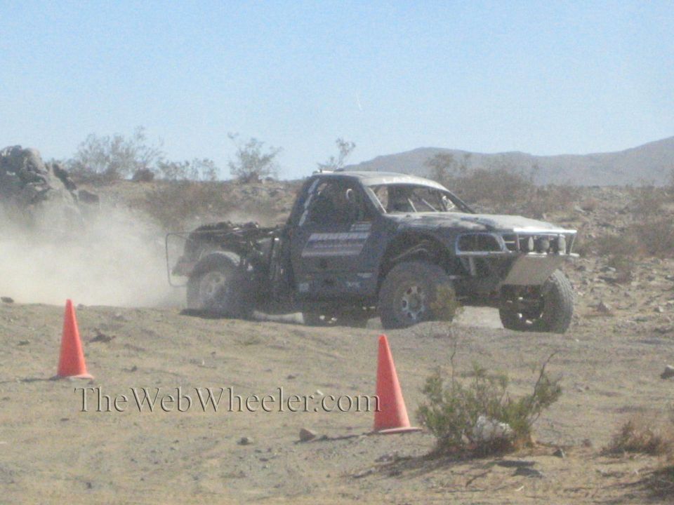 Silver and black off-road race truck side view on a desert course