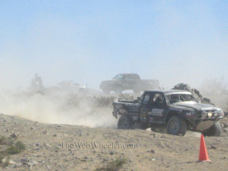 Off-road race truck in heavy dust with another truck behind in the desert