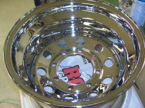 1974 Ford Bronco - A polished chrome wheel with a visible red 'R' logo and text on paper underneath.