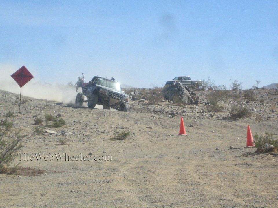 Lifted off-road truck climbing a desert hill past a warning sign