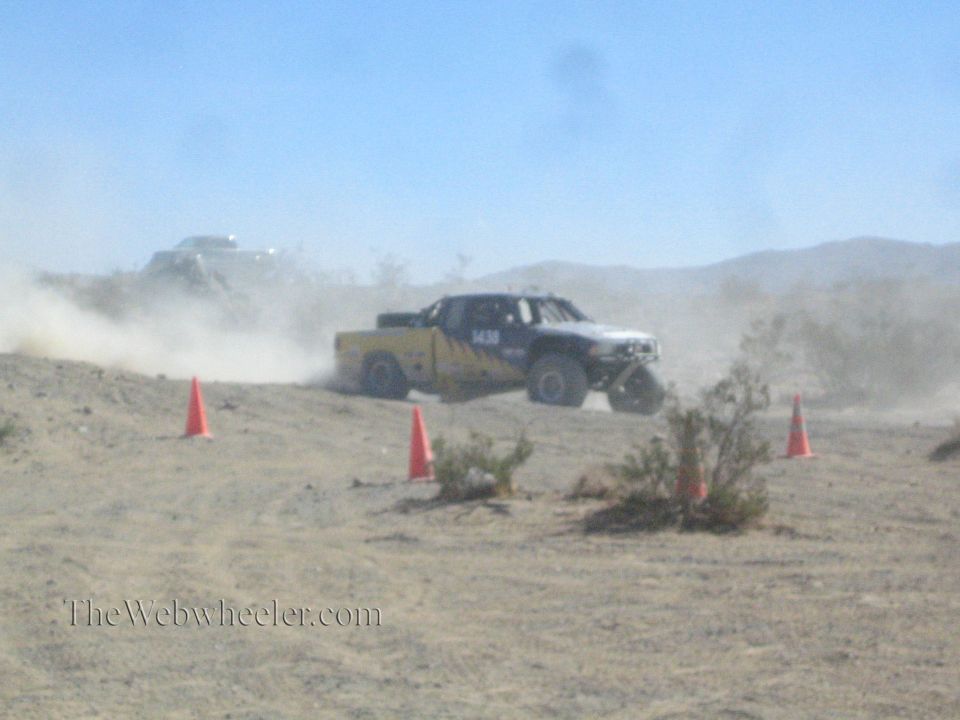 Yellow and white off-road race truck sliding through desert dust