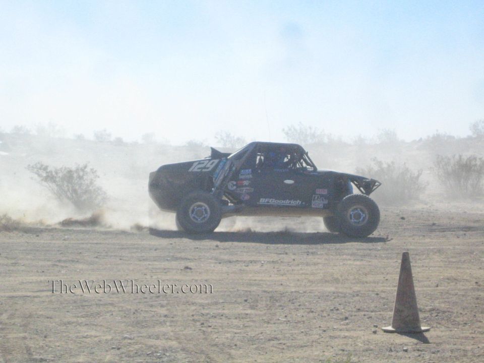 Black off-road race truck number 129 sliding through desert dust