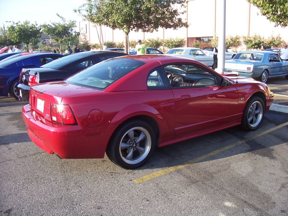 Red 2002 Ford Mustang parked in a lot with other cars. Rear quarter view