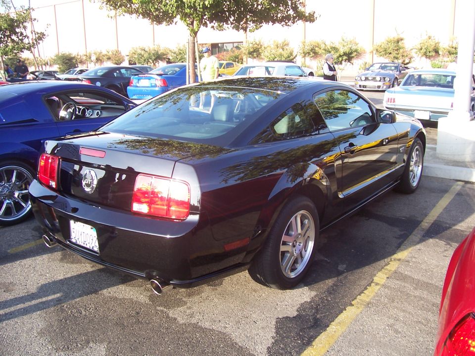 Black Ford Mustang coupe parked in a lot, rear-right view. Visible exhaust pipes and GT badge