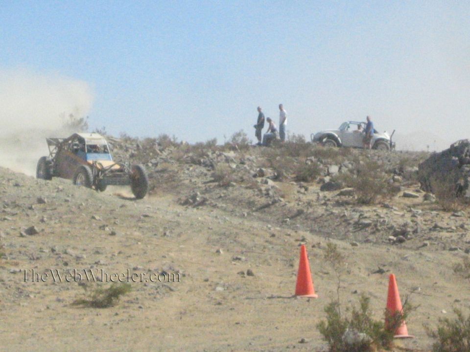 Open-frame off-road buggy on a rocky desert hill with spectators