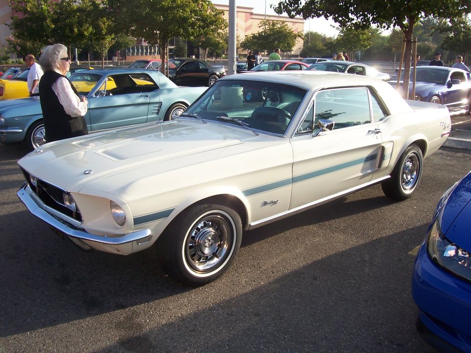 White 1967 Ford Mustang coupe with blue side stripes, chrome bumper, and aftermarket wheels