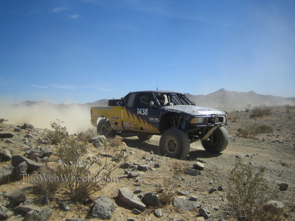 Blue and yellow off-road race truck number 1438 on a rocky desert trail