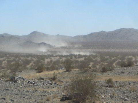 1990 Ford Bronco - distant dust plume rises from a vehicle racing across open desert scrubland toward low mountains.