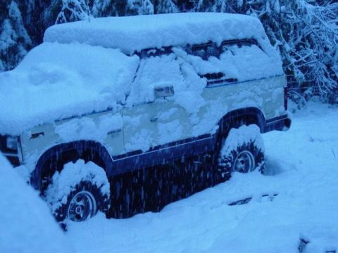 1986 Ford Bronco - A 1986 Ford Bronco is partially buried in snow, with only its side and front visible.