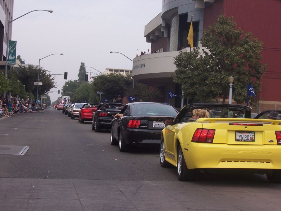 Yellow 2002 Ford Mustang convertible in a parade, rear view. License plate reads YM ROSE