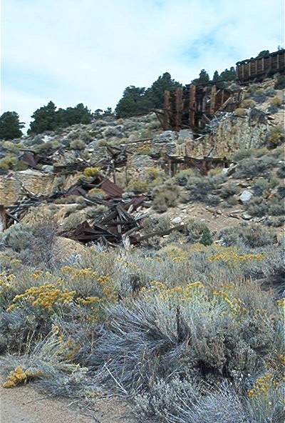 1986 Ford Bronco - Remnants of an old mine sit on a hillside, overgrown with desert vegetation.