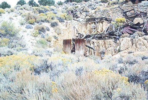 1986 Ford Bronco - Dilapidated mine structures stand against a rocky hillside, surrounded by arid vegetation.