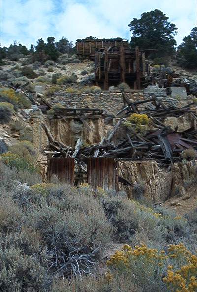 1986 Ford Bronco - Ruins of old mine structures are visible on a rocky, brush-covered hillside under a cloudy sky.