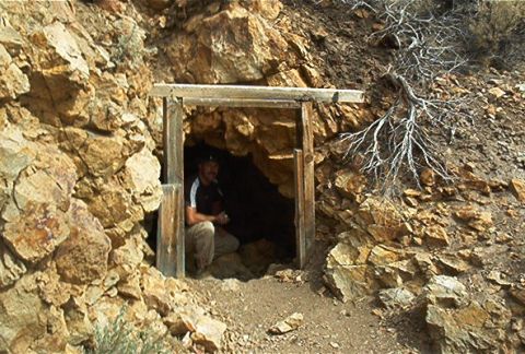 1986 Ford Bronco - A man is seen at the entrance of an old mine shaft, surrounded by rocks and dry brush.