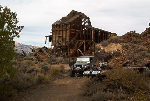1986 Ford Bronco - A Jeep Wrangler is parked near a dilapidated wooden structure in a desolate, mountainous landscape.